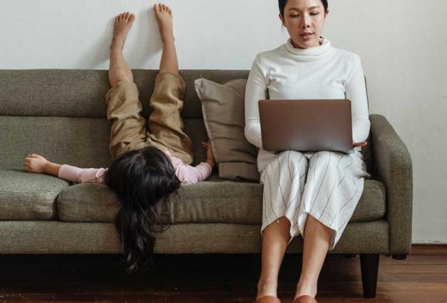 Woman working on laptop on sofa with daughter sitting next to her