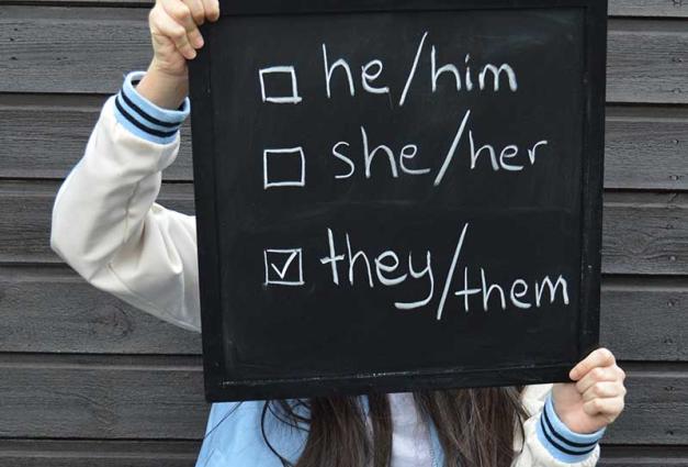 Person holding a sign showing different pronouns. 