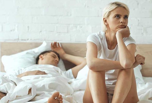 disappointed woman sitting on bed while boyfriend sleeping in background