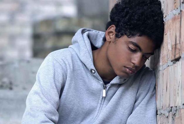 Depressed teenage boy leaning against wall