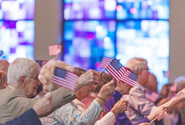 Senior parishoners holding small U.S. flags in a church