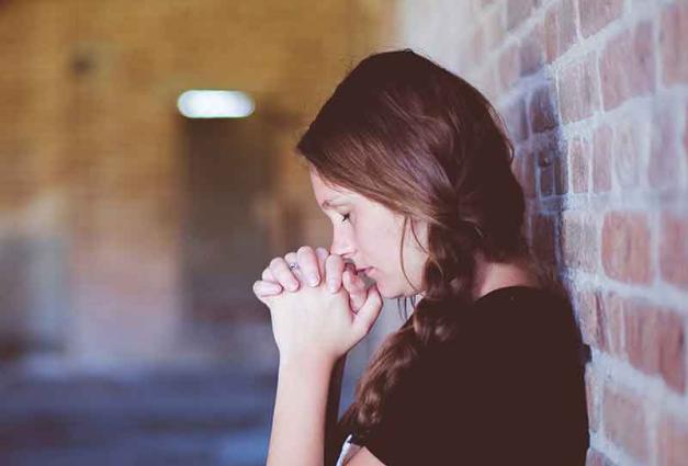 Young woman leaning against a wall praying