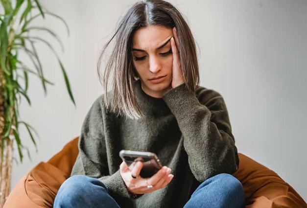 Distressed young woman sitting and looking at her mobile device