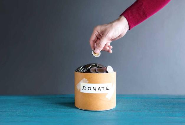 Hand adding coin to cup with the word Donate taped to the front