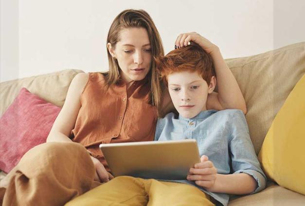 Mother and preteen son sitting on a couch looking at a mobile tablet 
