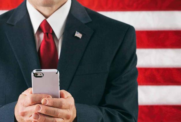 Male Politician Texting On Smart Phone in front of American Flag