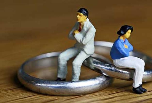 miniature toy people sit with arms crossed, backs to each other, on a pair of wedding rings.