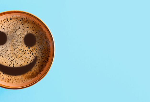 Cup of coffee on color background with smiley face in froth