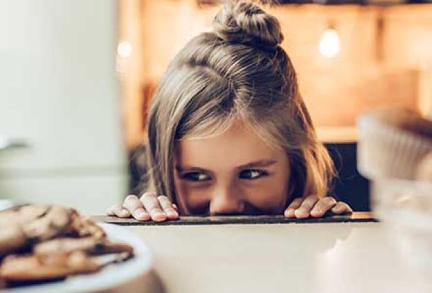 a small child peeks over a counter at a plate of cookies lurking nearby