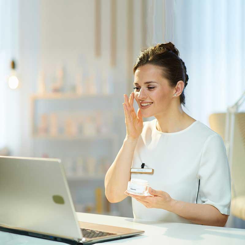 Woman checking makeup while looking at laptop screen