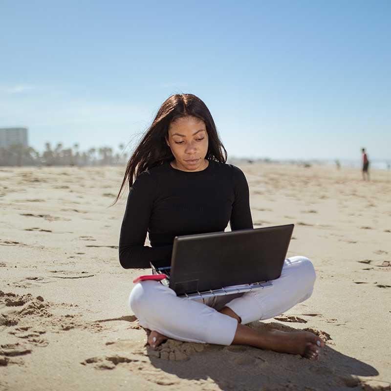 Young woman sitting on a beach working on a laptop