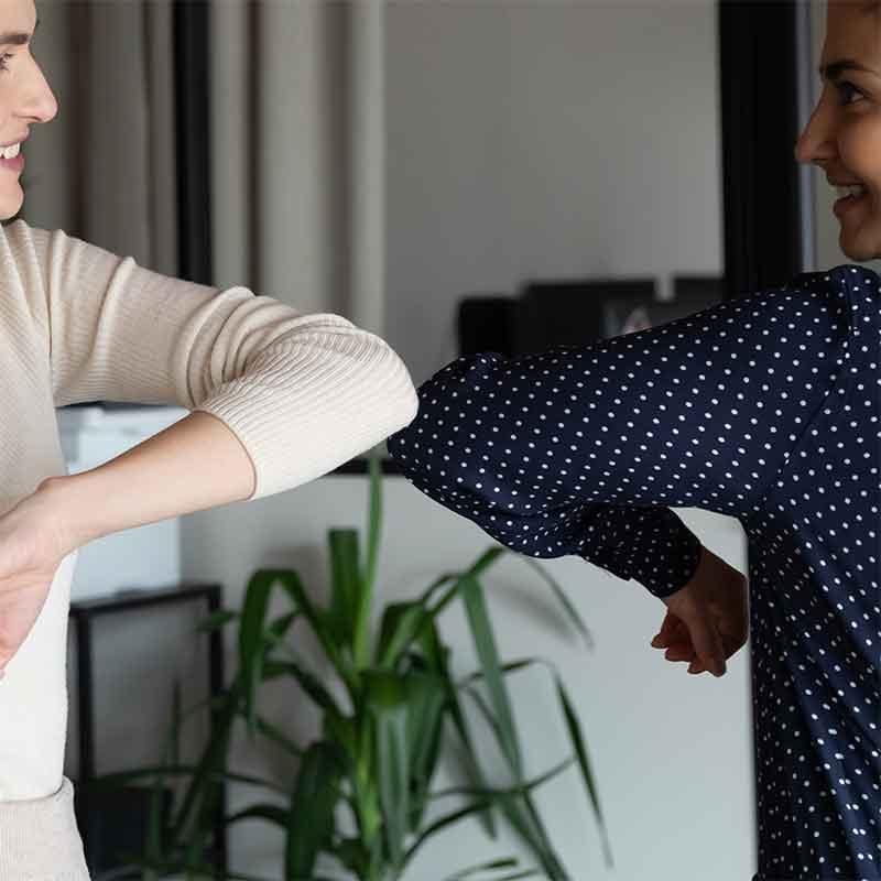Two young women elbow bump in office setting
