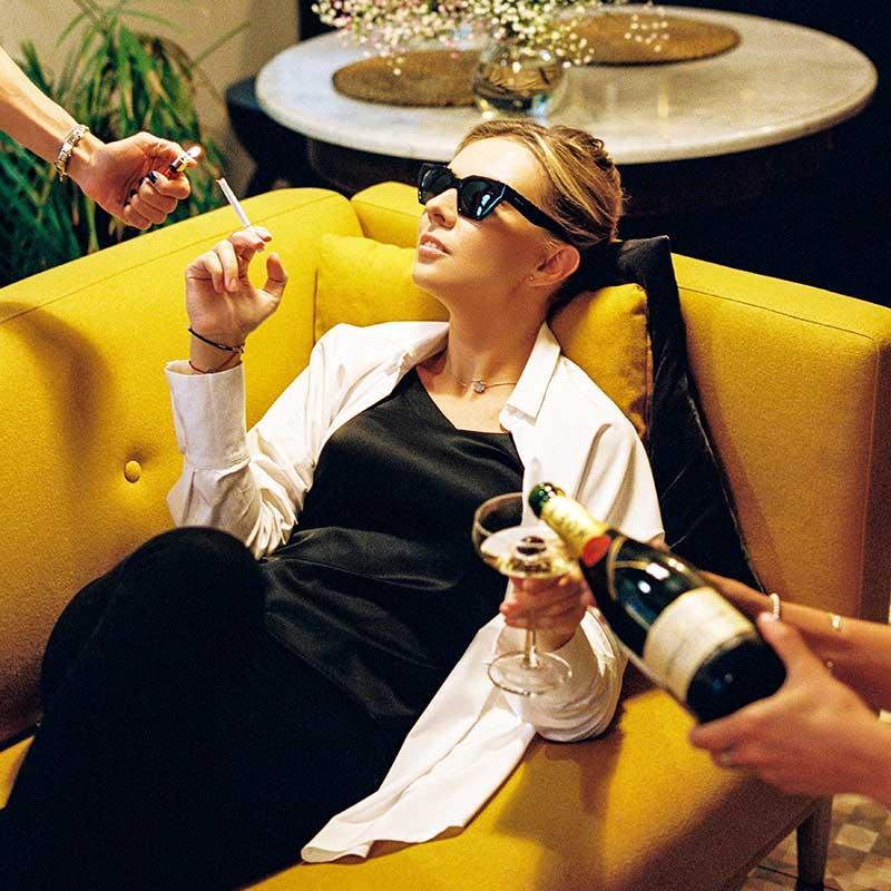 Woman lying on sofa having her cigarette lit and wine poured