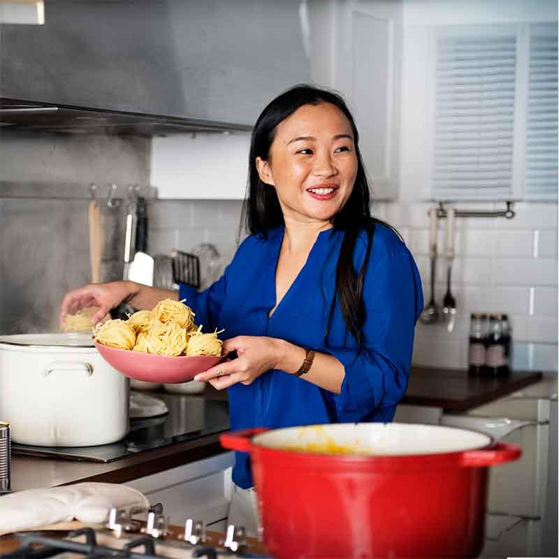 Asian woman cooking noodles in her kitchen