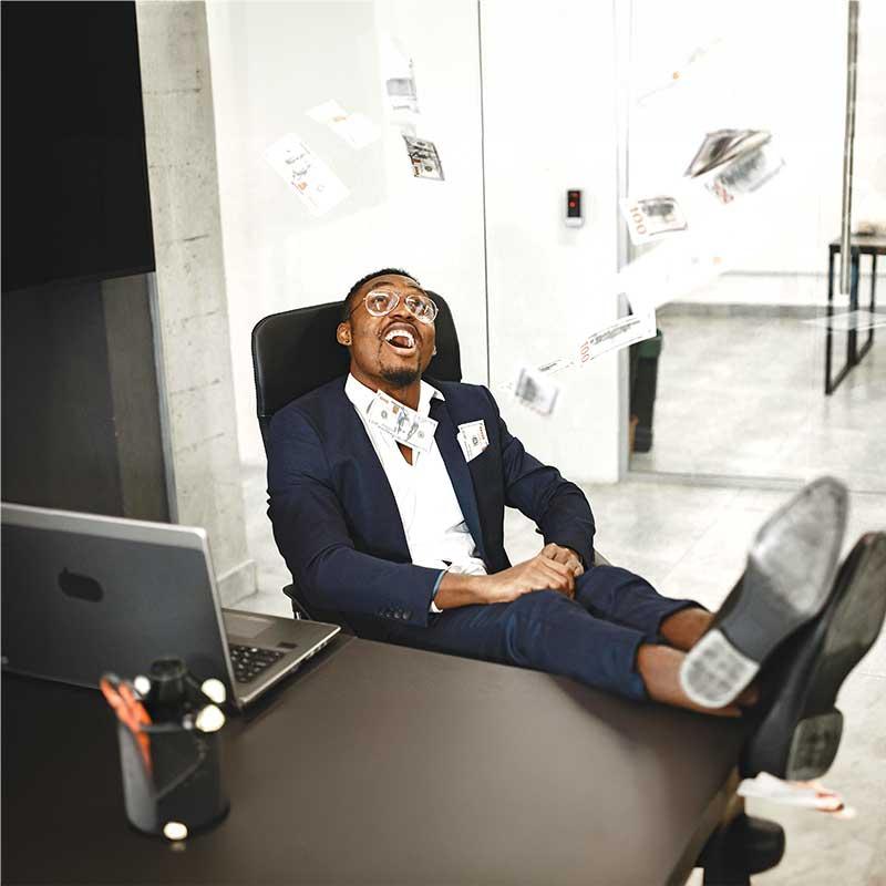 Man sitting with feet up on desk throwing money into the air