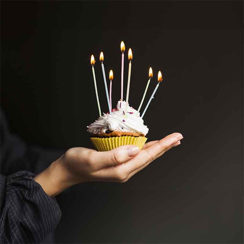 Hand holding a cupcake decorated with lit candles