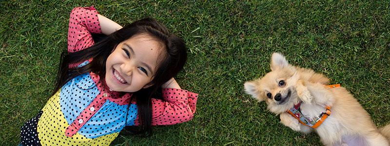 Young Asian girl lying on grass with her small dog