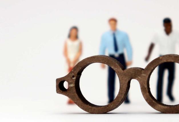 Group of adults in minature form standing behind a pair of glasses