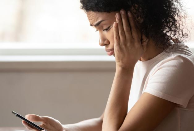 Young woman looking at mobile phone screen looking upset