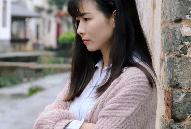 Young woman leaning against wall with arms folded and sour expression