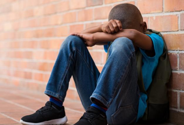 Young Black Student sitting on ground with his head in his hands