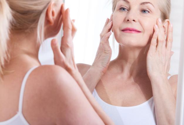 Middle aged woman looking in mirror while touching her face