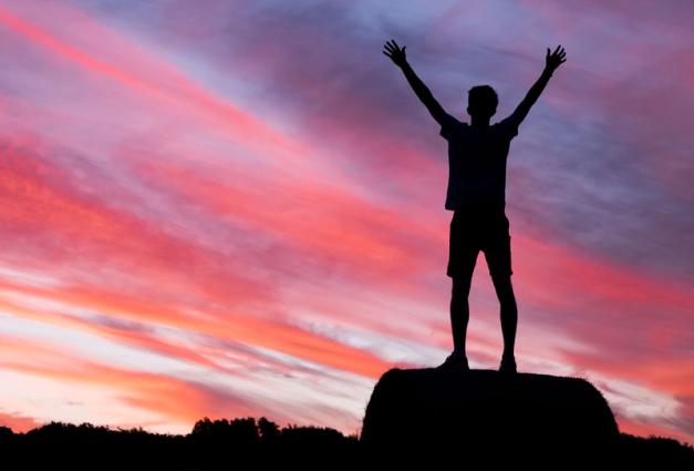 Silhouette of man standing on mountaintop with arms raised above his head