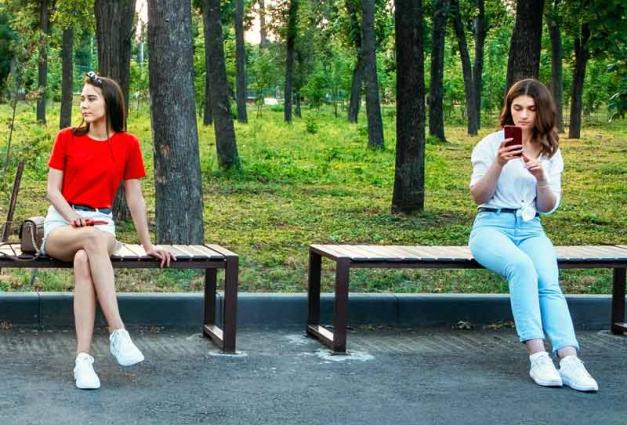 Two young women sitting on benches with space in between 