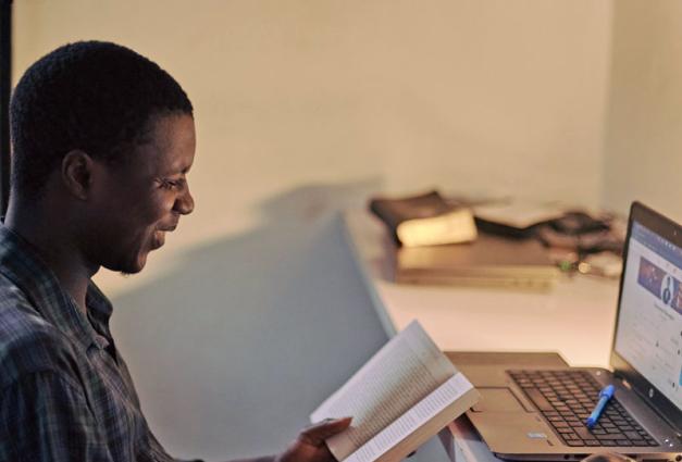 Young man sitting at desk looking at a book and a laptop