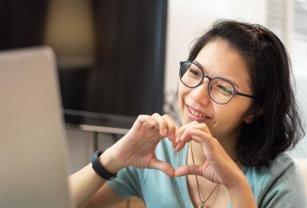 Woman making heart shape with hands in front of laptop