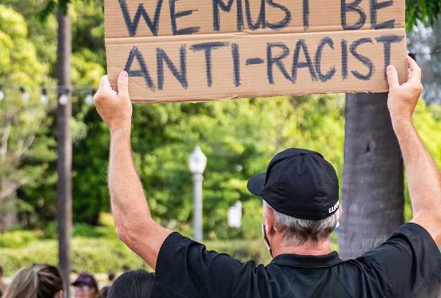 "We must be anti-racist" sign held by a man at a protest