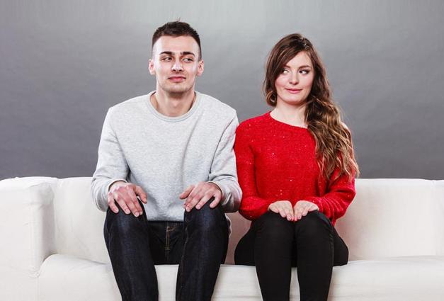 Young couple sitting a white sofa looking at each other with sideways glances