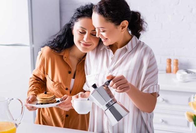 Hispanic same sex couple cuddling in kitchen having breakfast