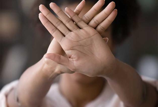 Black woman gesturing "stop" with hands overlapping and covering her face