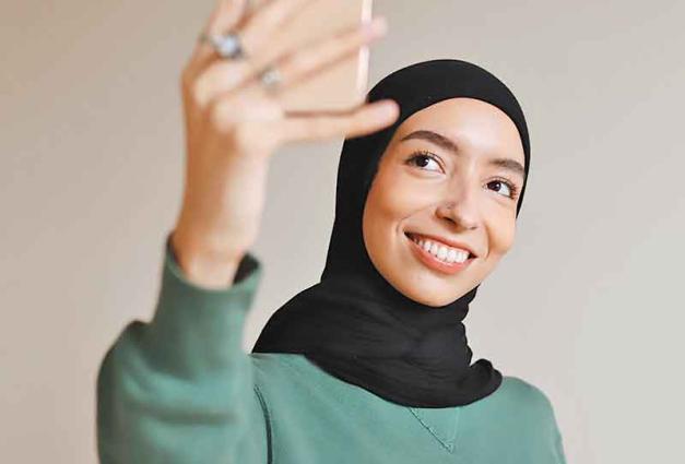 Woman in hijab smiling and taking selfie