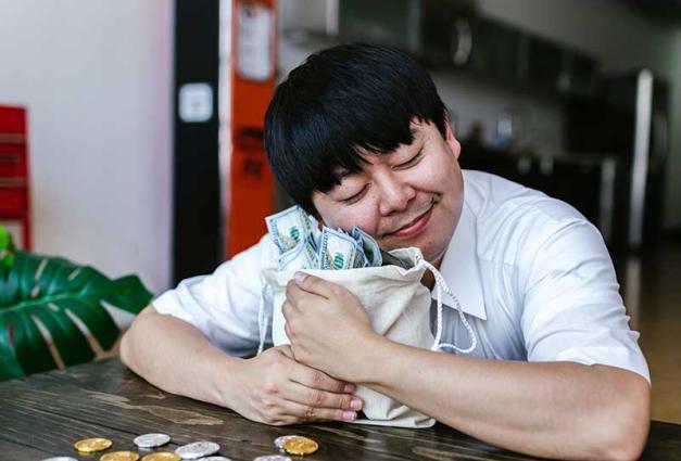 Man sitting at a table smiling and hugging a bag of money 