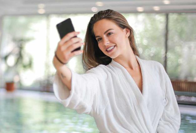 Woman wearing white robe taking selfie near swimming pool