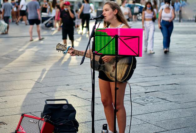 Female busker playing a guitar on a city street