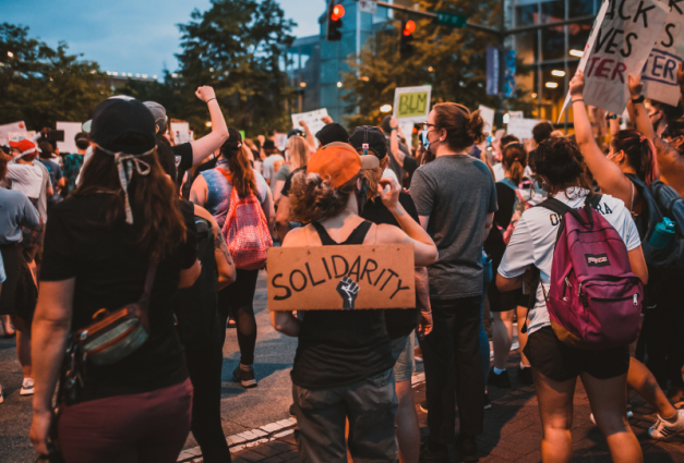 A group of people stand in a street, protesting with fists raised.