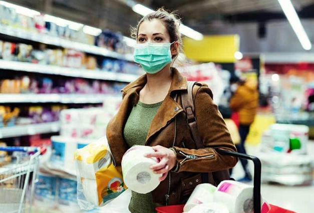 Woman with face mask making stock of toilet paper while buying in supermarket.