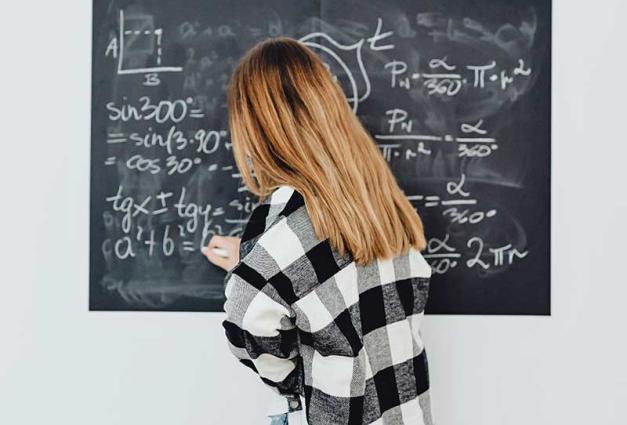 Young female student writing math computations on chalkboard