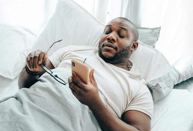 Black man lying in bed looking at his mobile device