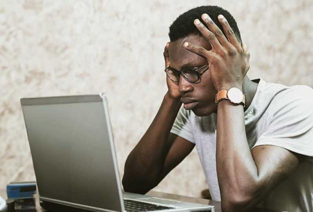 Man holding his head in his hands looking at a laptop