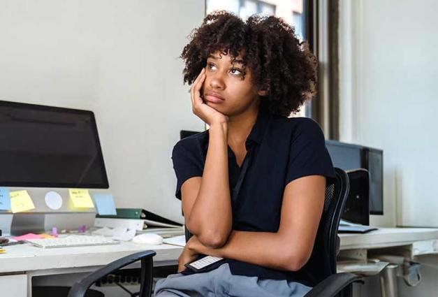 Young woman sitting at desk thinking and staring into space