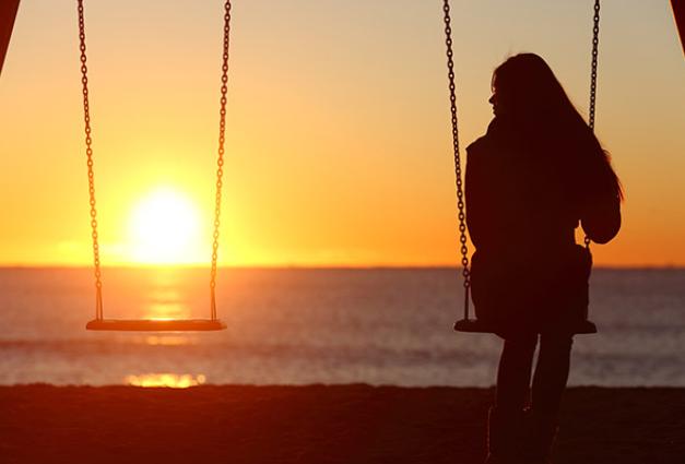 Image of young woman on a swing by herself looking at the sunset