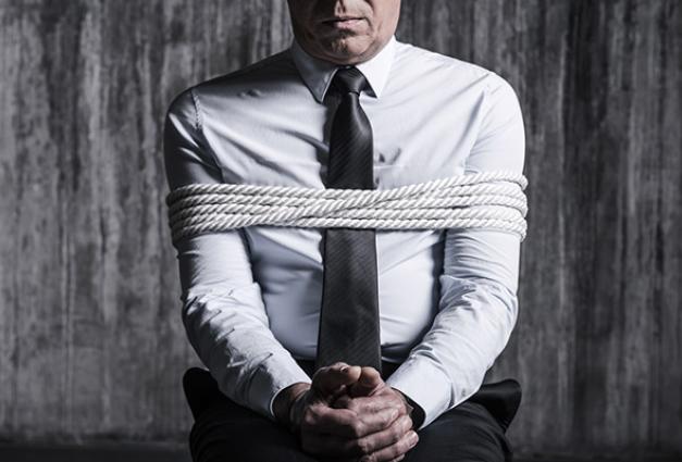 Image of a man in a dress shirt sitting down tied up with rope