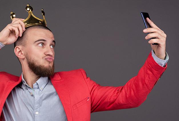 Young man wearing gold crown taking selfie with smartphone