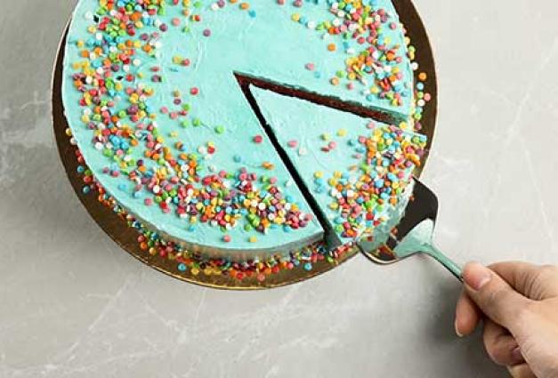 Person taking slice of fresh delicious colorful cake at table, top view