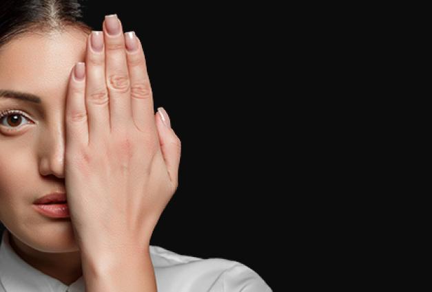 Asian brunette woman in a white shirt covering her face with her hand on a black background