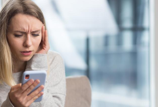 Stressed Young woman sitting at home on the couch looking at mobile phone